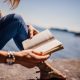A picture of a lady reading a book in the sunshine by the water