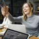 Picture of a lady at her desk with a laptop smiling happily as someone approaches to shake her hand. Show two people engaging in a happy friendly relationship.