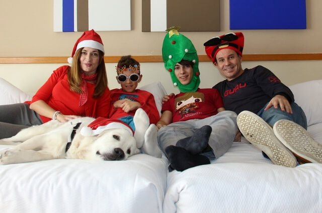 Image of a family sitting on a bed wearing silly christmas hats.