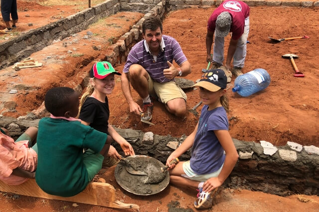 Picture of a man and children helping to build a school in Kenya