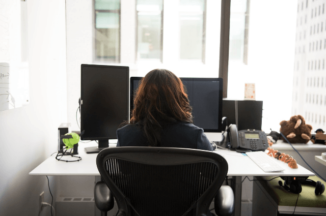 Picture of a female worker sitting at her desk starring at her computer looking bored