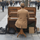 Picture of a man player a piano in the street amongst a busy crowded market