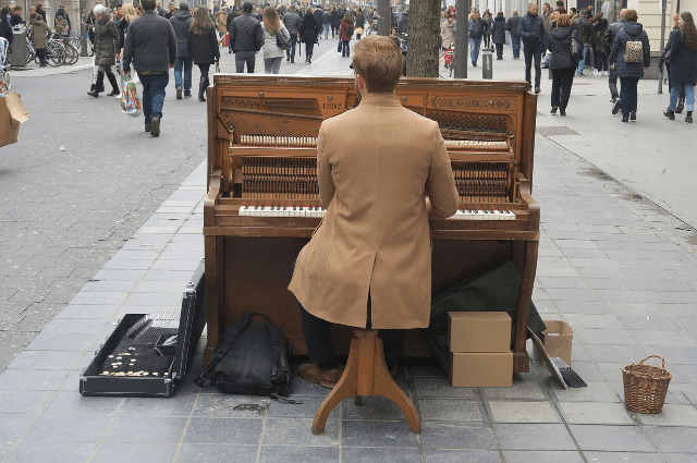 Picture of a man player a piano in the street amongst a busy crowded market