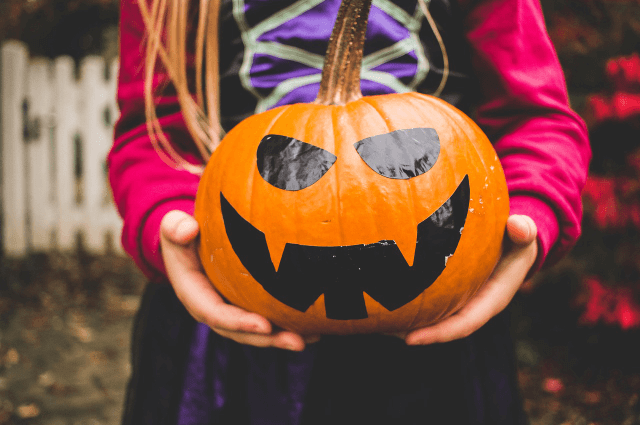 Picture of a girl dressed in as a witch holding a jack o lantern for Halloween