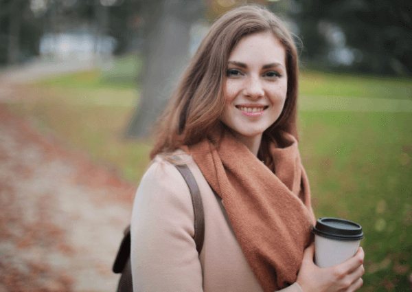 Image of a woman holding a take away coffee cup outside in the autumn