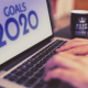 A picture of a man typing on a laptop with the words 2020 goals on the screen