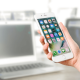 Picture of man holding a white smart phone in front of a computer