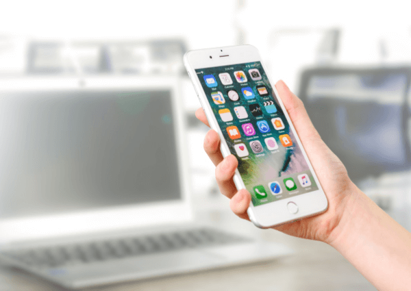 Picture of man holding a white smart phone in front of a computer