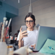 A business woman selling painting supplies is sitting at her desk with a laptop and a mobile phone