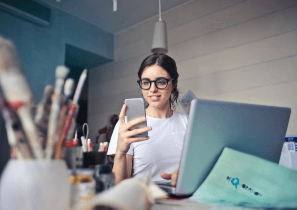 A business woman selling painting supplies is sitting at her desk with a laptop and a mobile phone