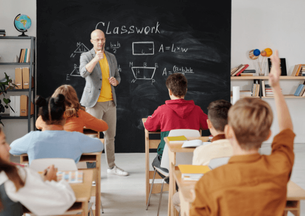 Image of a teacher standing at a blackboard teaching school children