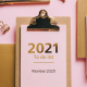 An image of a clipboard and office stationery on a pink background. The clipboard reads 2021 to do list review 2020