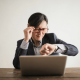 Image of a business man sitting at his laptop checking the time on his watch