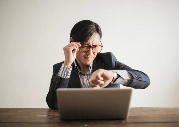 Image of a business man sitting at his laptop checking the time on his watch