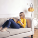 Picture of a woman sitting on the couch in her living room reading a book and relaxing