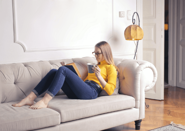 Picture of a woman sitting on the couch in her living room reading a book and relaxing