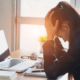 Picture of a woman at her desk, head in hands.