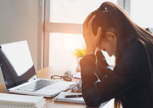 Picture of a woman at her desk, head in hands.