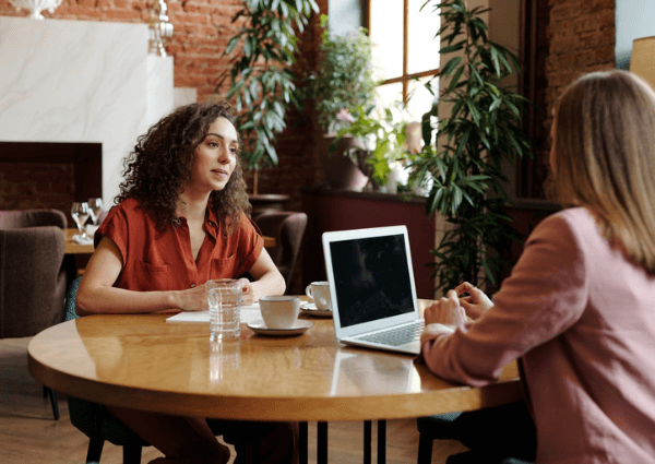 two women sitting at a table in a coffee shop conducting an interview