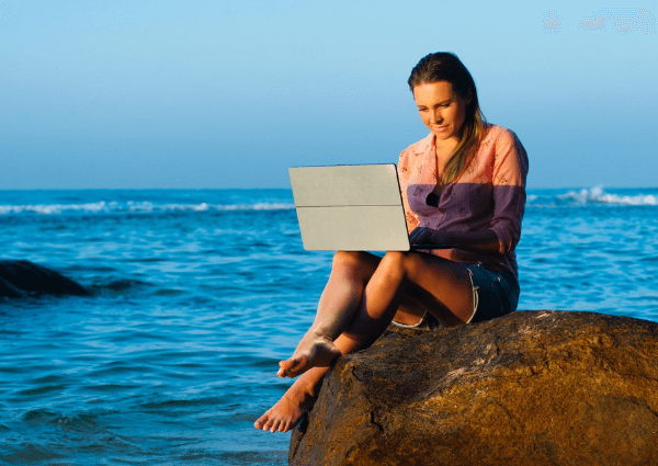 Woman sitting on a rock with a laptop close to the sea