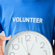 Image of a man wearing a blue t-shirt with the words volunteer and holding a white clock