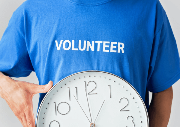 Image of a man wearing a blue t-shirt with the words volunteer and holding a white clock