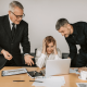Picture of a business woman at her laptop being disrupted by two colleagues