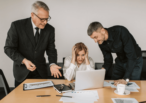 Picture of a business woman at her laptop being disrupted by two colleagues