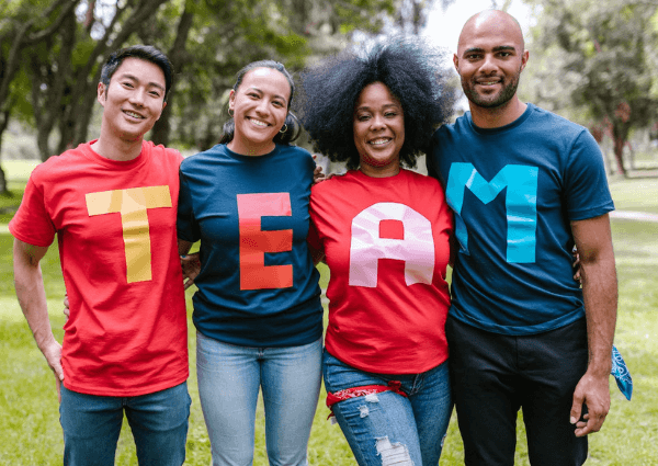 Four team members standing together wearing a t-shirt each with a letter that spells team