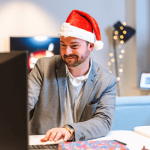 Picture of a man sitting at a computer in the office wearing a Christmas hat