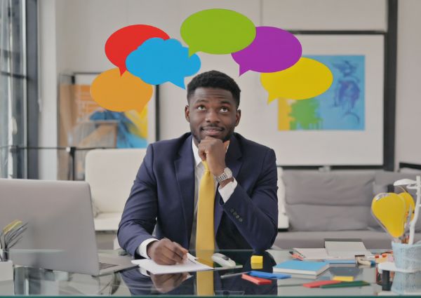 Business man sitting at his desk with speech bubbles above his head